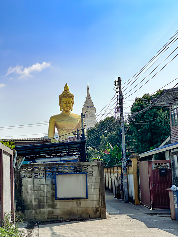 Stock photo showing  view from fence lined alleyway of Phra Buddha Dhammakaya Thep Mongkol, a bronze plated giant Buddha statue by Wat Paknam Bhasicharoen a royal temple, Bangkok, Thailand.