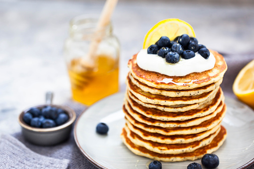 Stack of freshly prepared lemon poppy seed pancakes topped with sour cream and blueberries