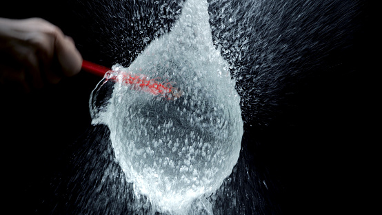 Water balloon exploding or splashing which represent power of refreshing or freshness for viewer and blasted by pencil in hand on black background in the studio.