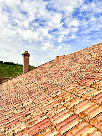 Tiled roof of a building with a chimney against the background of a blue cloudy sky. Architecture of Europe. Vertical image.
