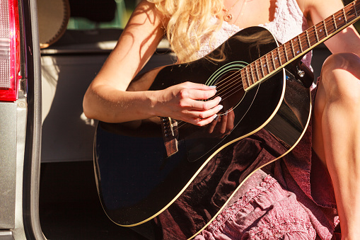 Travel vacation hitchhiking concept. Summer girl hippie style sitting on hatchback car with acoustic guitar