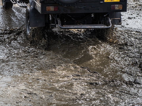 Off-road Jeep car on bad gravel road. Mud and water splash in off road racing. Off-road travel on mountain road