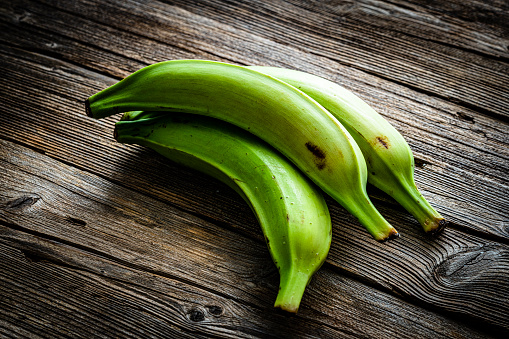 Three green plantains on wooden table