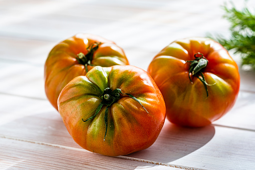 Tasty ripe tomatoes sliced on chopping board with greenery, sharp knife near, isolated over dark background. Kitchenware. Top view.
