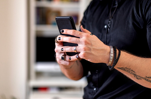 Tattooed arms and painted fingernails of a muscular man. Young adult man using smart phone to pay bill, to make online payment service or online shopping. Cashless payment using mobile application and make money transfer completely via internet.