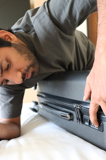 Stock photo showing close-up view of a grey wheelie suitcase on a double bed mattress covered in fresh bedding. The case with a zipper has a combination lock needing to be opened by rotating numbered discs to form a three digit sequence.