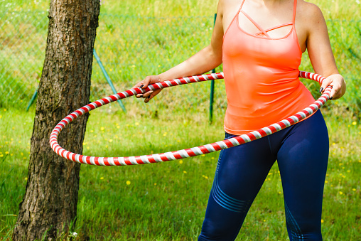 Woman using hoola hoop for slim fit body, doing exercises gym outdoor in garden. Workout training on fresh air. Active healthy lifestyle.