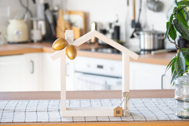 istock Key and tiny house of cozy home with Easter decor with color eggs on table of kitchen. Building, design, project, moving to new house, mortgage, insurance, rent and purchase real estate 2117171833