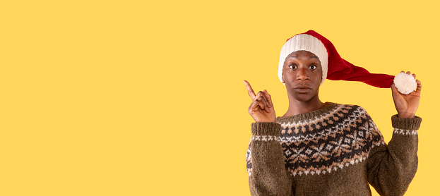 cheerful christmas woman in christmas sweater and santa hat getting thumb up on yellow background. Merry Christmas and happy new year concept