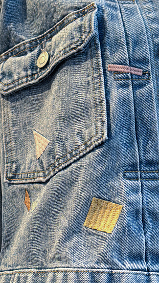 Stock photo showing close-up view of embroidered shapes on denim jacket pocket.