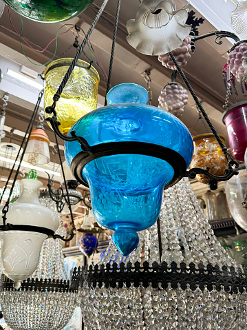 Stock photo showing illuminated, coloured glass lanterns and lamps suspended from ceiling in interior lighting store in shades of blue and green.