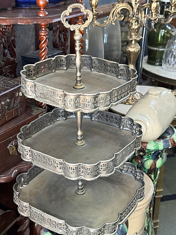 Stock photo showing close-up view of antique shop items including silver cake stand,  cabinet, tables, glassware and stoneware bed warmer.
