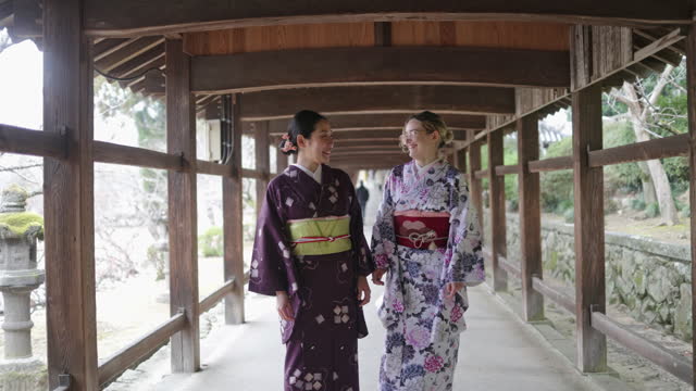 Female friends in kimono talking and looking at camera in the shrine corridor - slow motion