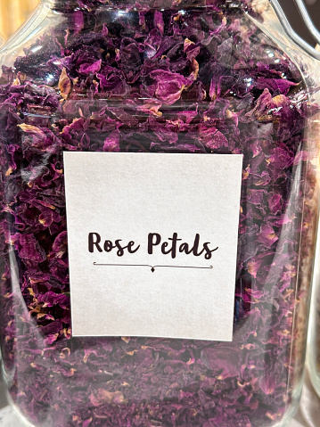 Stock photo showing close-up view of labelled glass jar containing  fragrant, natural, plant potpourri made from dried red-pink rose petals.