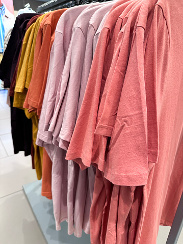 Stock photo showing close-up view of some multicoloured T-shirts hanging on a clothes rail in a clothing department store .