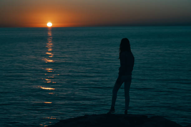istock woman near the sea at sunset dark silhouette and beach model 2117286607