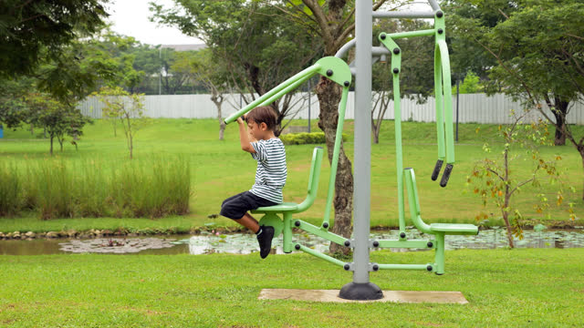 Boy attempts to exercise on outdoor pull-down challenger, designed for adults