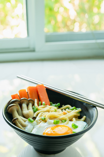 delightful Asian noodle bowl featuring soft-boiled eggs, mushrooms, and carrots, perfect for a flavorful breakfast or lunch served with chopsticks in a vertical composition.