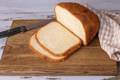 Пшеничный (белый) хлеб с хрустящей корочкой на деревянной доске, нарезанный ломтиками. Домашняя выпечка в стиле рустик. Выборочная фокусировка, крупный план.