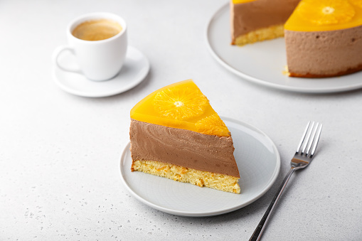 Шоколадно-апельсиновый муссовый торт с бисквитной основой, желе и кружочками апельсина. Кусок домашнего чизкейка и чашка кофе. Традиционны