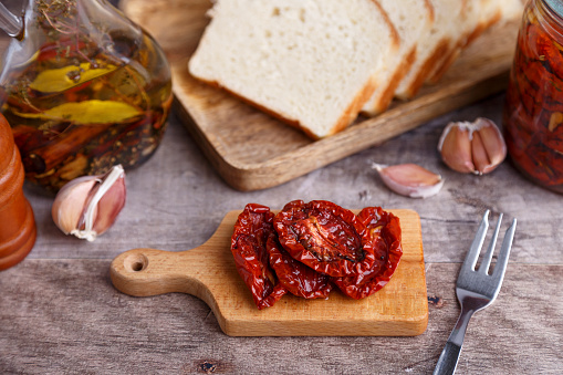 Вяленые помидоры в оливковом масле на мини-доске с домашним хлебом в деревенском стиле. Традиционная домашняя кухня. Выборочная фокусировка, крупный план.