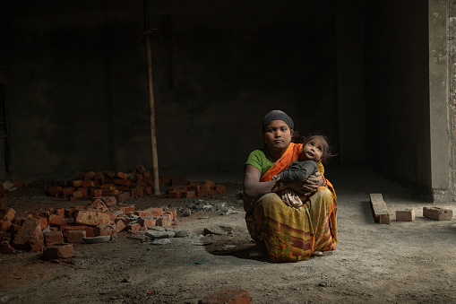 Portrait of mid adult mother dressed in sari holding daughter and sitting inside building while working at construction site