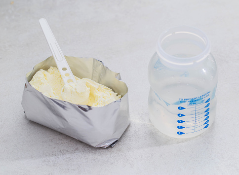 A baby feeding bottle and a measuring spoon with a handful of dry baby formula for preparing milk for the baby. Useful and healthy food, close-up.