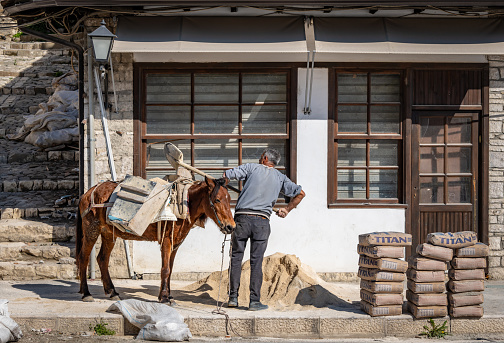 Berat, Albania. 15 March 2024. A man loads sand on to a horse in Berat old town.