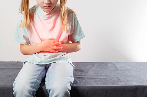 A seven-year-old girl sits and holds her red belly with her hands. Concept of abdominal abdominal pain in children. Enterovirus infection and poisoning. Treatment of abdominal pain in children. Copy space for text, jaundice