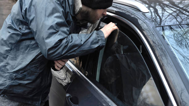 istock Homeless thief steals purse valuable items from car with unlocked doors open. Property insurance against unlawful theft or crime. Male burglar looks through crack in window. Auto without alarm system 2117373382