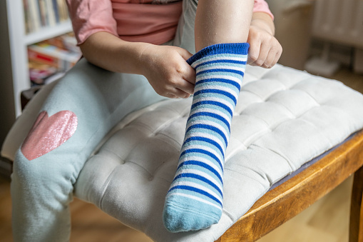 close-up of female 4-year-old child, Preschooler learning to dress independently, putting on blue striped sock, Young kid achieving self-dressing milestones, Fine motor development, Self-care skills