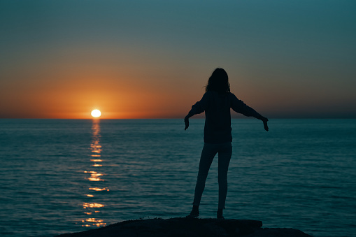 silhouette of a woman at sunset near the sea gesturing with hands back view. High quality photo