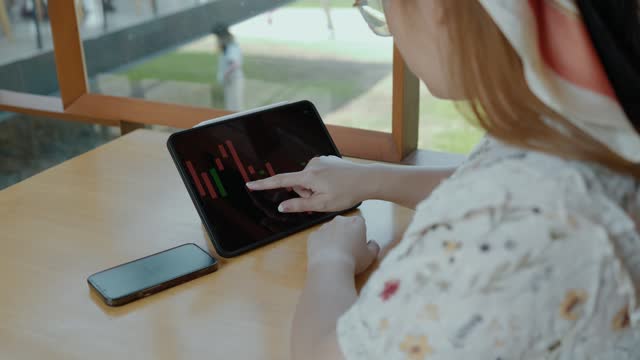 A female investor is looking at stock charts to analyze profitable trades, trading stocks on the stock market platform, she sits in a coffee shop and analyzes the stock market.