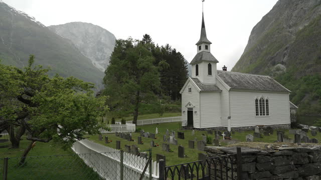 traditional old fashioned white wooden stave church in the beautiful and tranquil landscape at the Naeroyfjord in Norway with snow covered mountains in the background.
