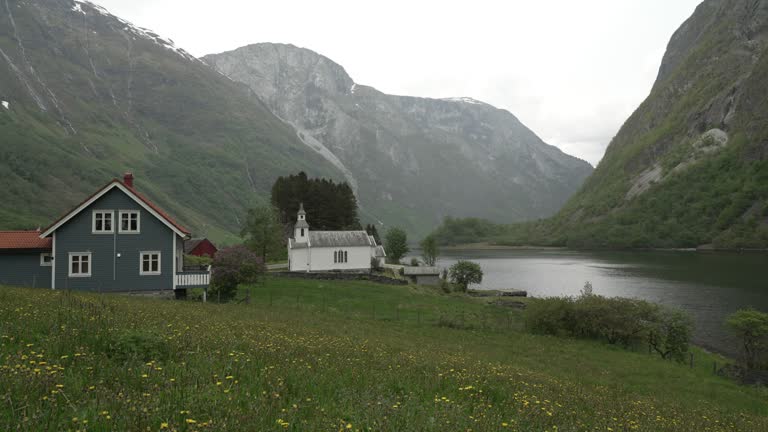 traditional old fashioned white wooden stave church in the beautiful and tranquil landscape at the Naeroyfjord in Norway with snow covered mountains in the background.