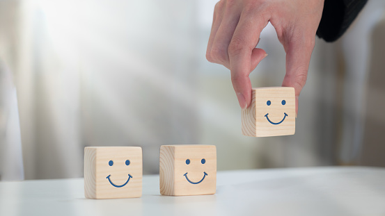 A happy smile is painted on the face of a wooden block cube to symbolize optimism. notion of emotional and mental wellness;