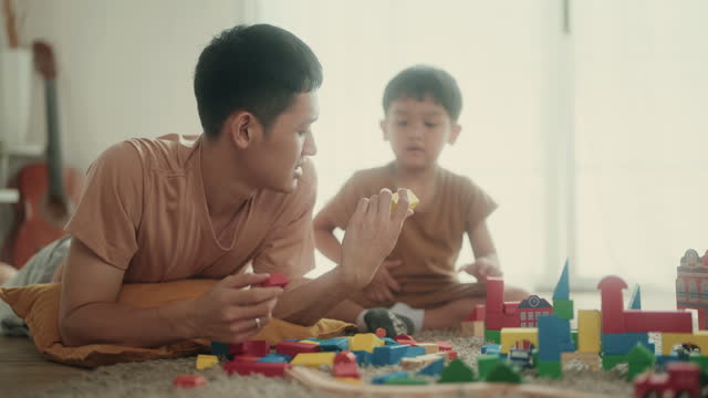 Cheerful Asian Dad and Toddler Son Enjoy Playtime with Toy Blocks in Cozy Home Setting | Parent-Child Fun and Learning.