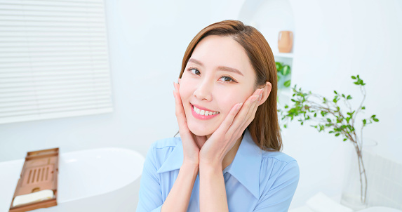 Closeup asian businesswoman looks mirror in bathroom -  she appreciates her facial skin feels happy and satisfied loving herself