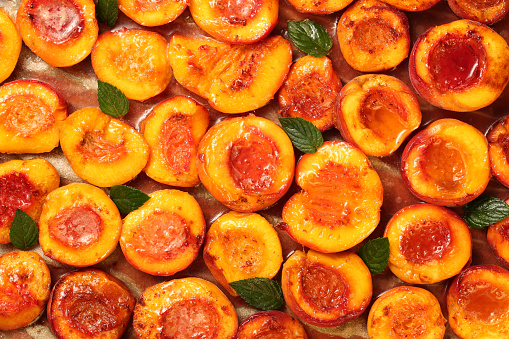 Top down view of healthy and delicious fruity dessert with half sliced peaches, baked with honey, cinnamon, butter and fresh mint leaves. Colorful food texture background.