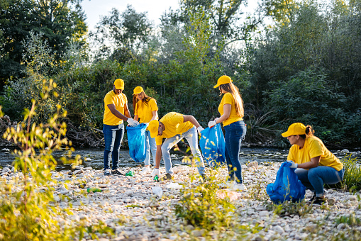 Group of young volunteers cleaning up garbage on the riverbank.