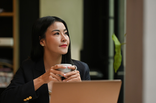 Thoughtful businesswoman hands holding coffee cup and looking away through the office window.
