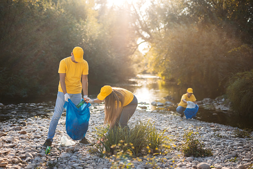 Group of young volunteers cleaning up garbage on the riverbank.