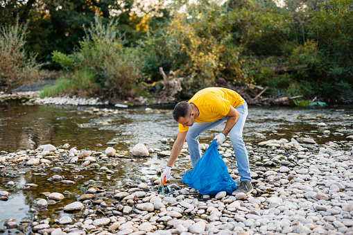 Young male volunteer cleaning up garbage on the riverbank.