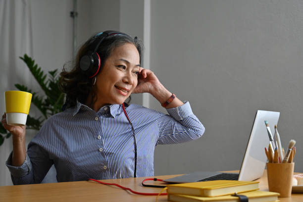 istock Smiling senior woman wearing headphone watching business training on laptop while remote working from home. 2117497931