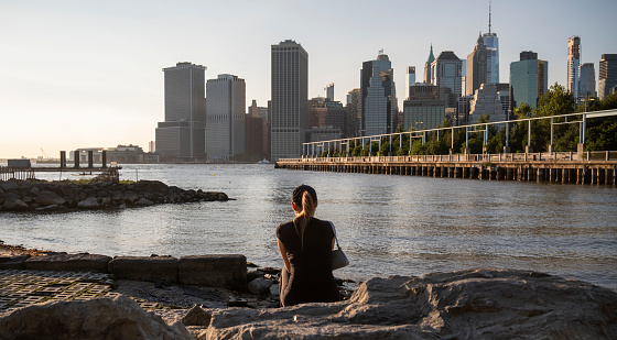 Serene Moment: Woman Overlooking the NYC Skyline by the Water