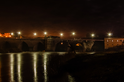 Paisaje nocturno con el Río Duero, puente medieval y el pueblo de Tordesillas al fondo.