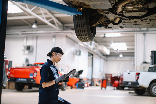 Female Japanese electrician mechanic in a car repair shop, inspecting vehicles, doing the regular maintenance and oil change.