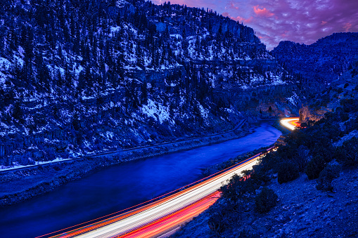 Night View Glenwood Canyon During Blue Hour - Twilight views of scenic canyon along the Colorado River with vehicle lights trails during long exposure. Interstate 70 in Colorado looking west. Night driving transportation through scenic rugged canyon.