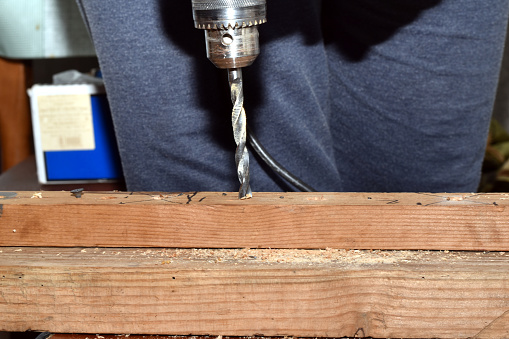 Close-up of a drill being used to make a hole in a board.