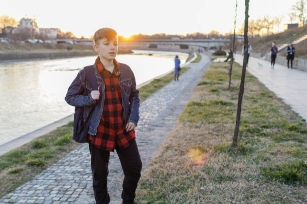 Cute boy is walking near the river at sunset.